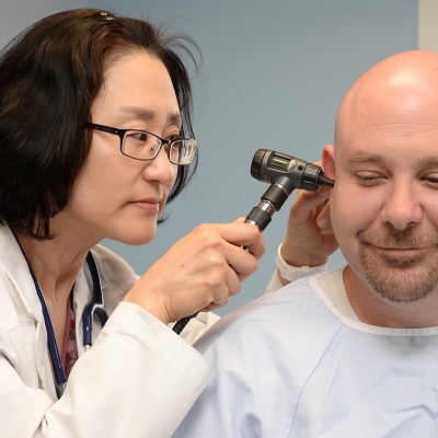 Asian NP checking ear of white male patient.